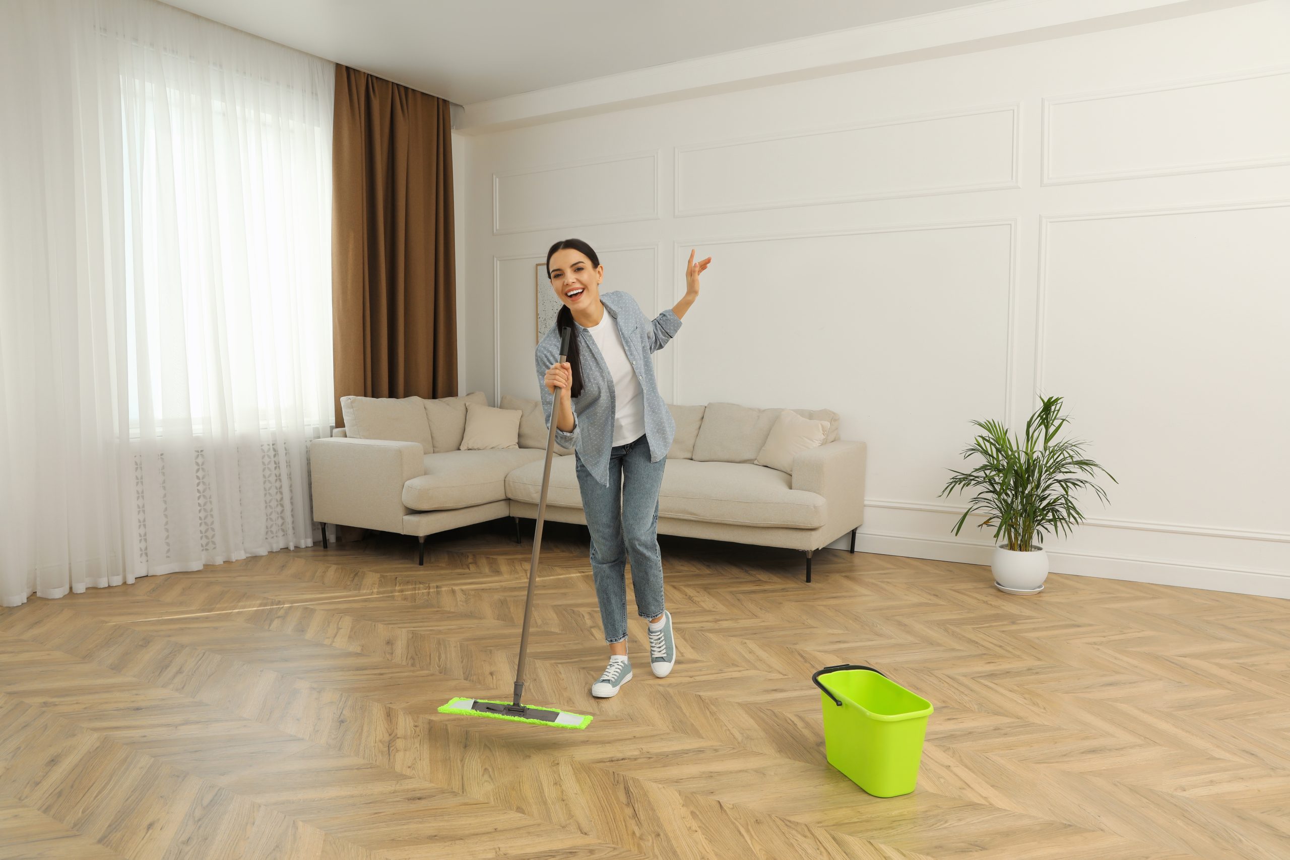 Restoring parquet floors in Harrow – homeowner doing aftercare with a microfibre mop on a herringbone oak parquet wood floor in a bright living room.