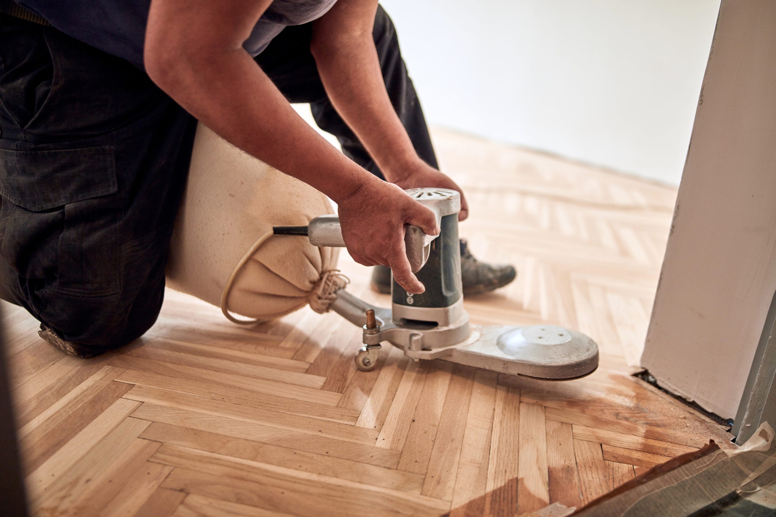 Restoring parquet floors in Harrow – professional edge sanding of a herringbone oak parquet wood floor with a dust-extraction bag at a doorway.