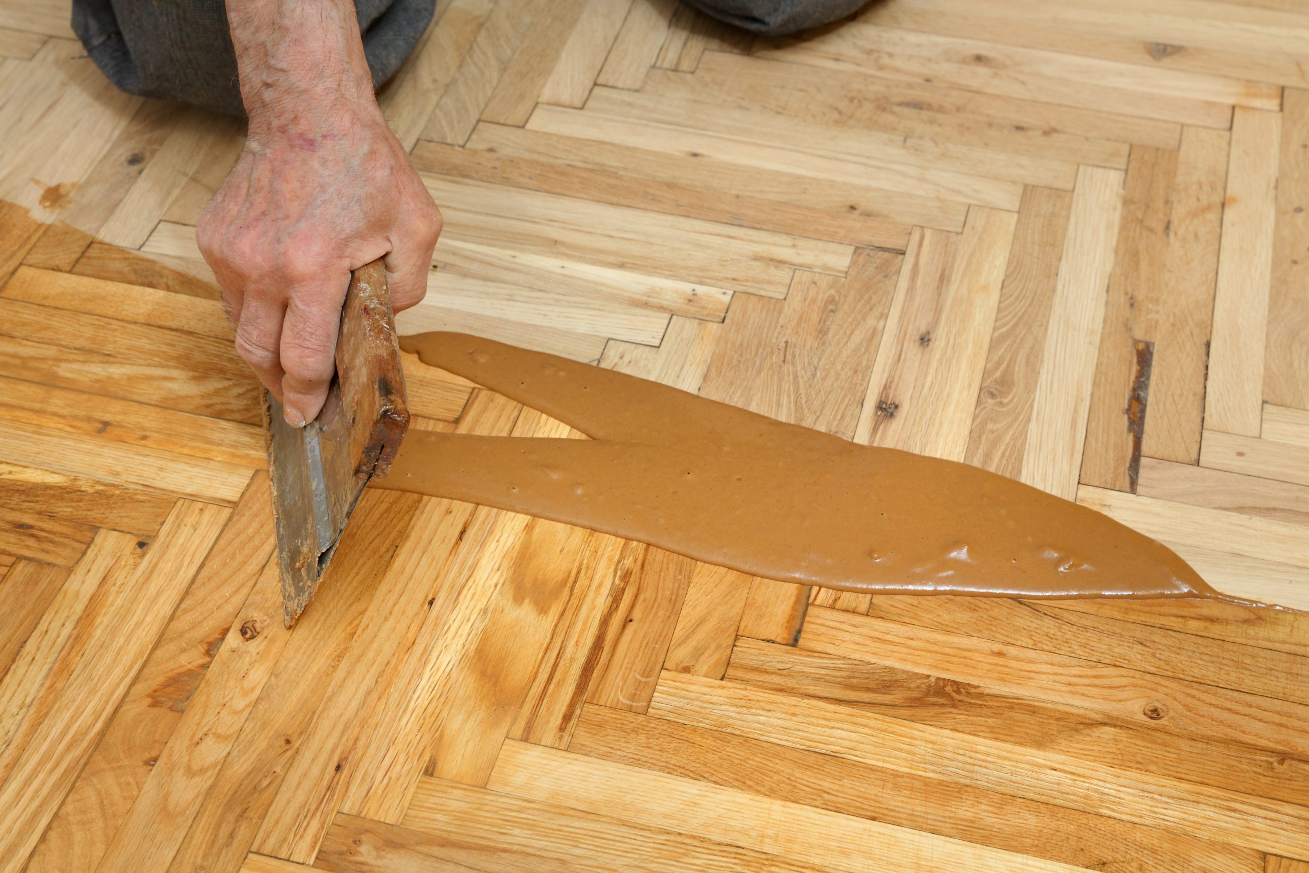 Restoring parquet floors in Harrow – resin gap filling on a herringbone oak parquet wood floor during sanding and repair.