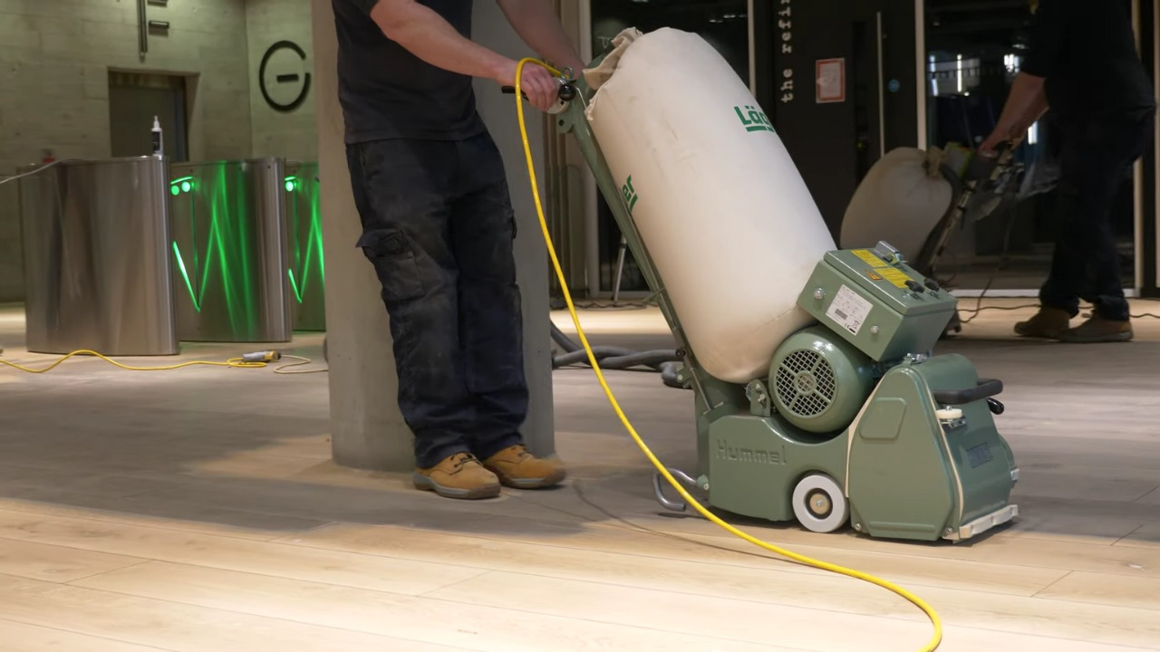 Parquet Floor Sanding in Harrow on a commercial light oak hardwood floor, with a technician operating a large dust-extraction sanding machine in a modern building.