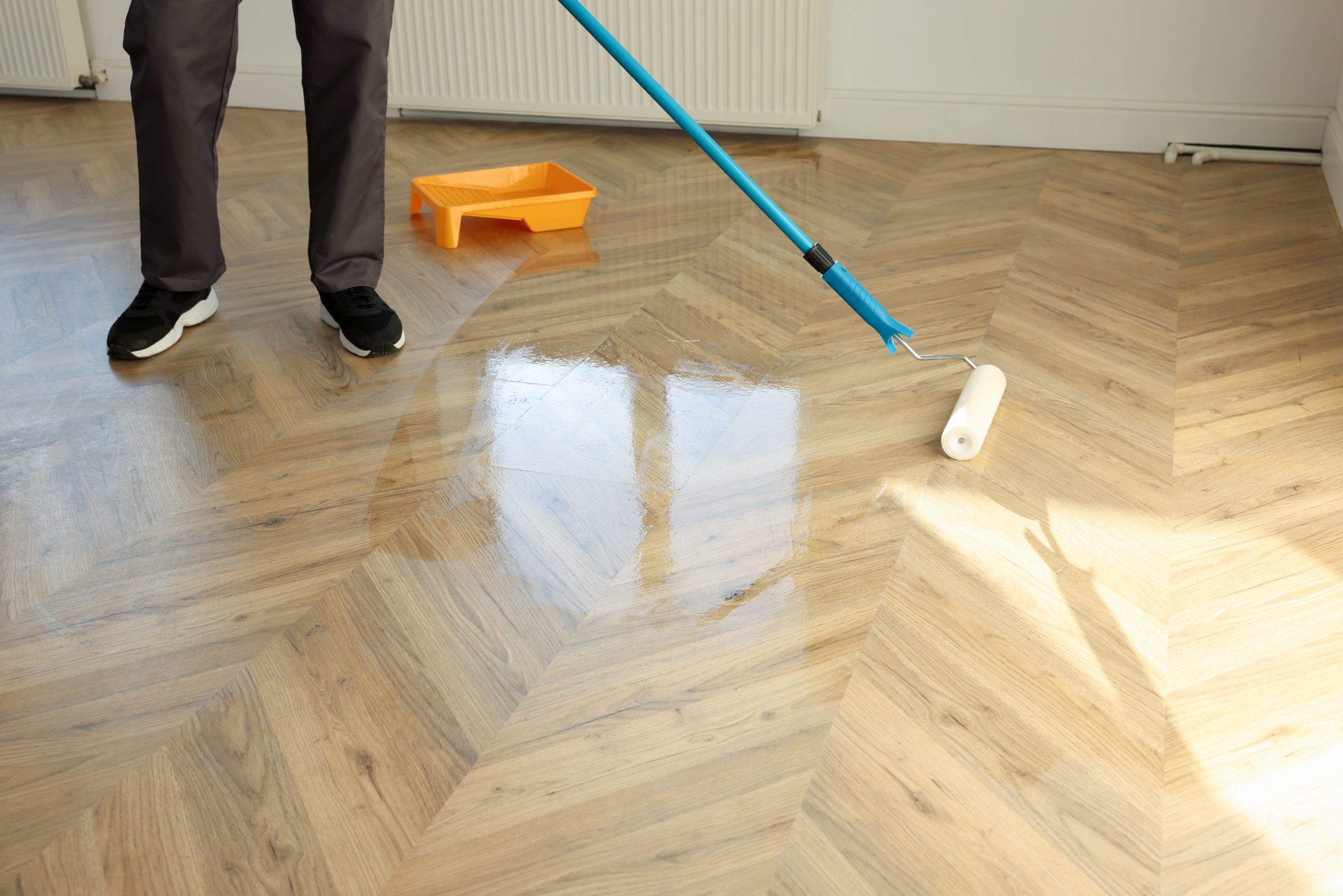 Parquet Floor Sanding in Harrow with a technician applying clear lacquer to a newly sanded light oak chevron parquet wood floor using a roller.