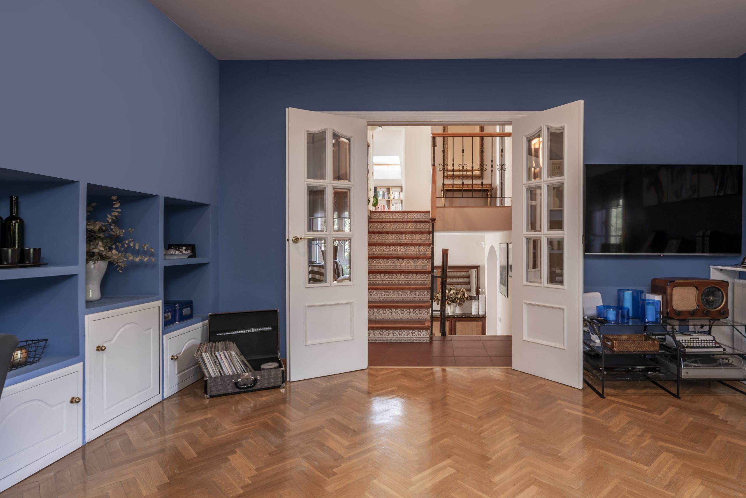 Parquet Floor Sanding in Harrow on a medium oak herringbone parquet wood floor in a stylish blue living room with white doors opening onto stairs.