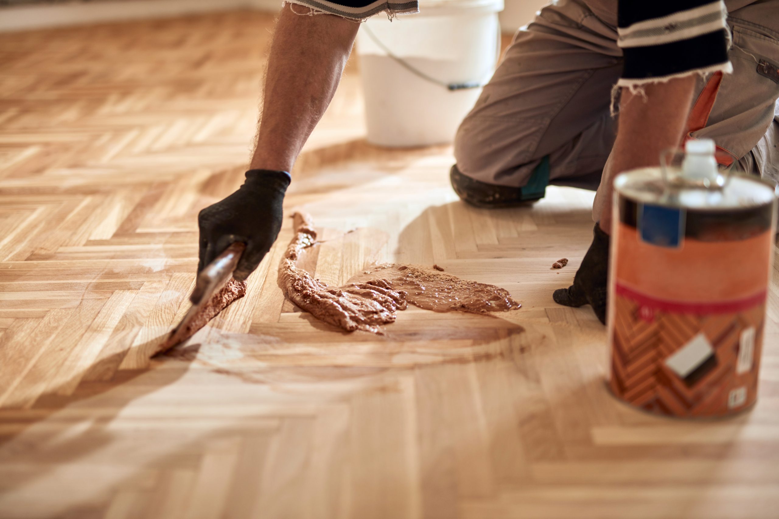 Parquet Floor Sanding in Harrow with a technician filling gaps on a newly sanded light oak herringbone parquet wood floor before sealing.
