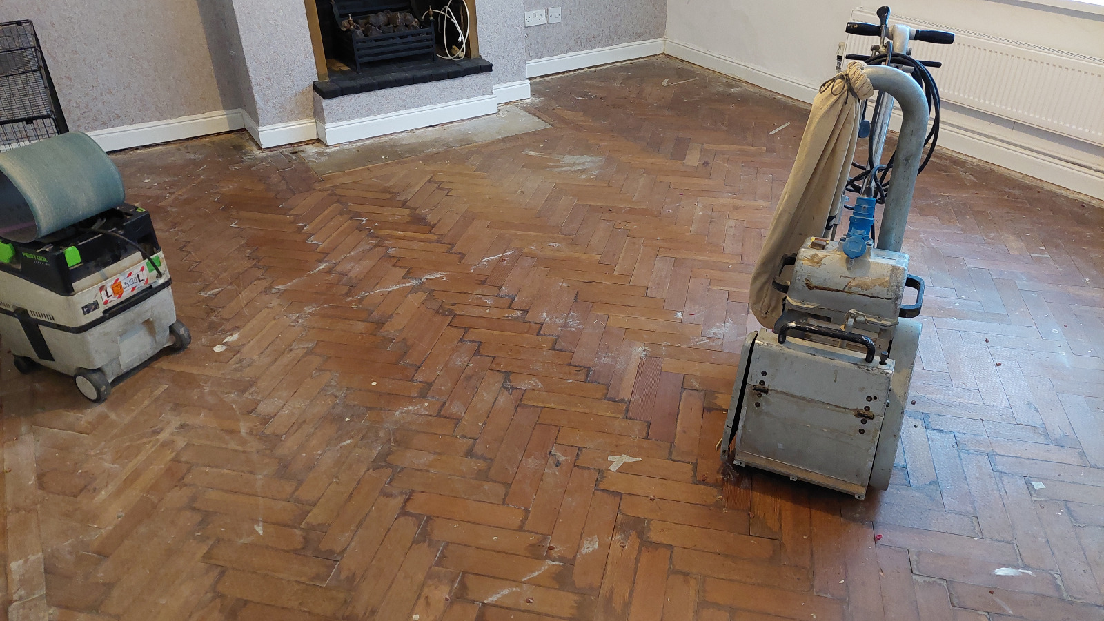 Parquet Floor Sanding in Harrow on a worn oak herringbone parquet living room floor, with professional sanding machines set up before restoration.