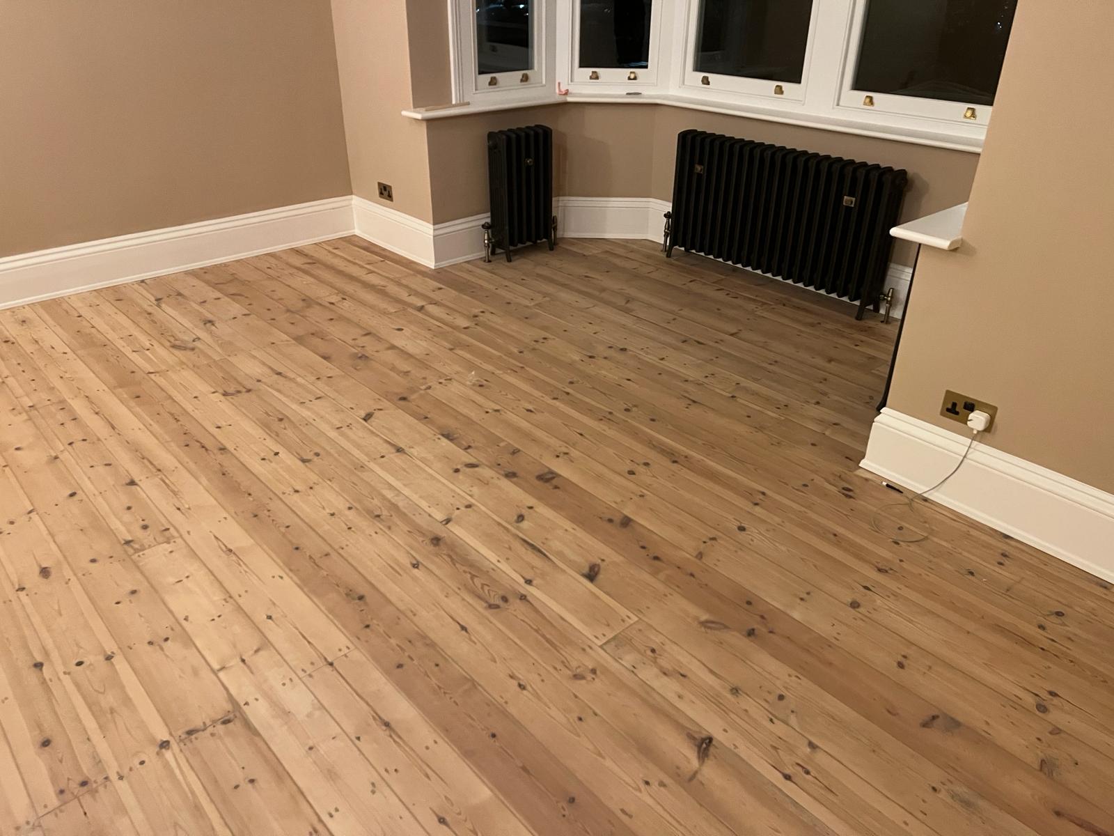 Completed Wood Floor Sanding in Harrow, showing smooth solid pine floorboards with a natural matt finish in a bay-fronted room.
