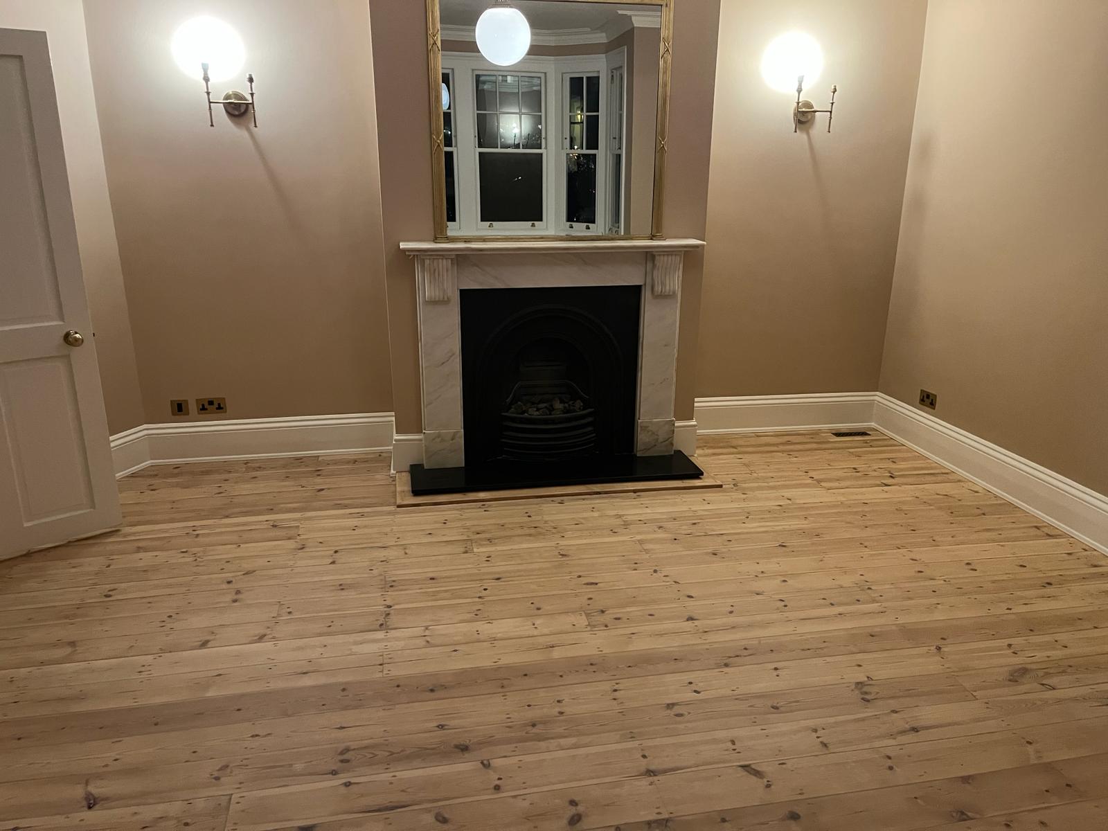 Freshly restored living room after Wood Floor Sanding in Harrow, showing pale solid pine floorboards around a period fireplace.