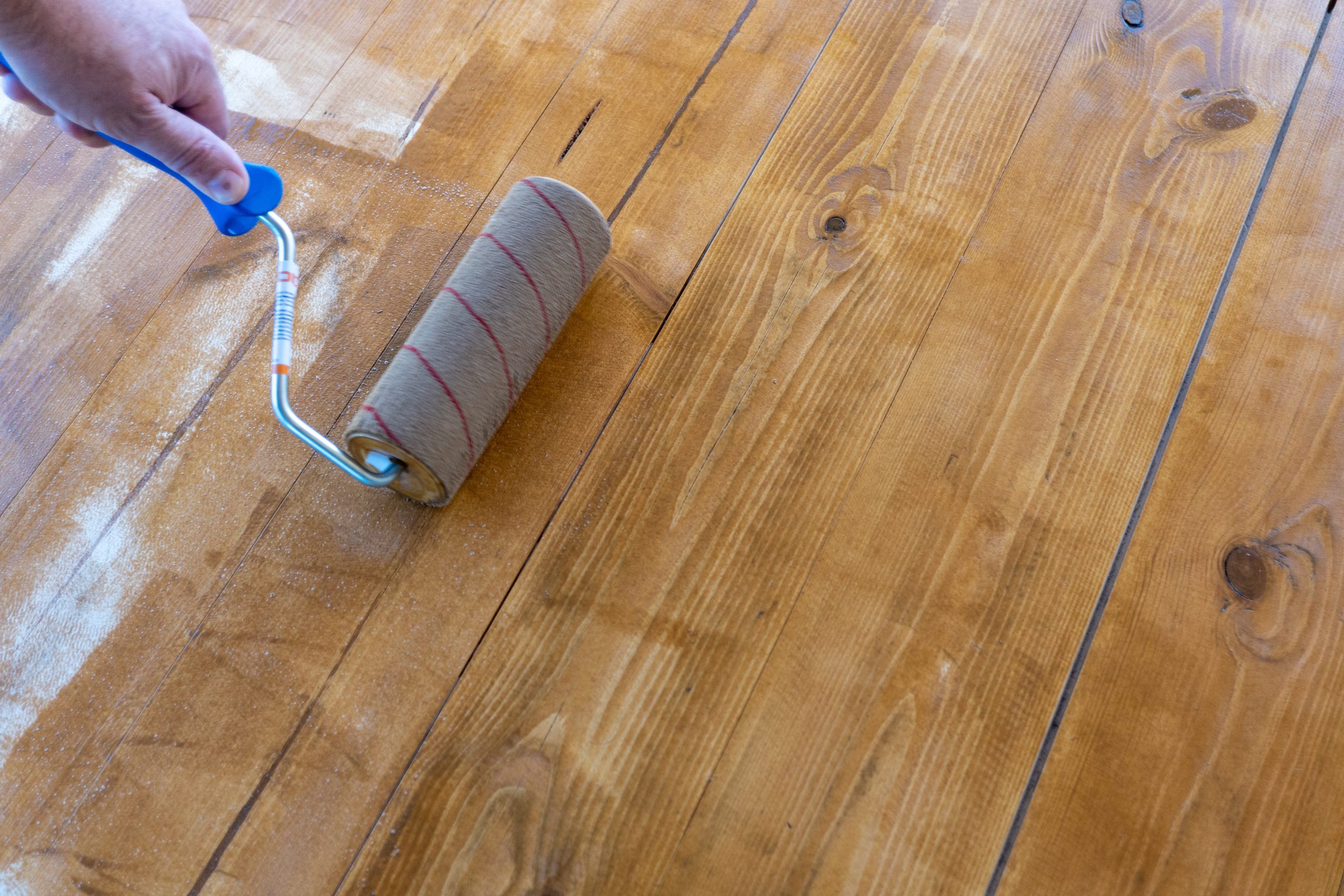 Applying finish after Wood Floor Sanding in Harrow on solid pine softwood floorboards with a roller for a smooth, even seal.